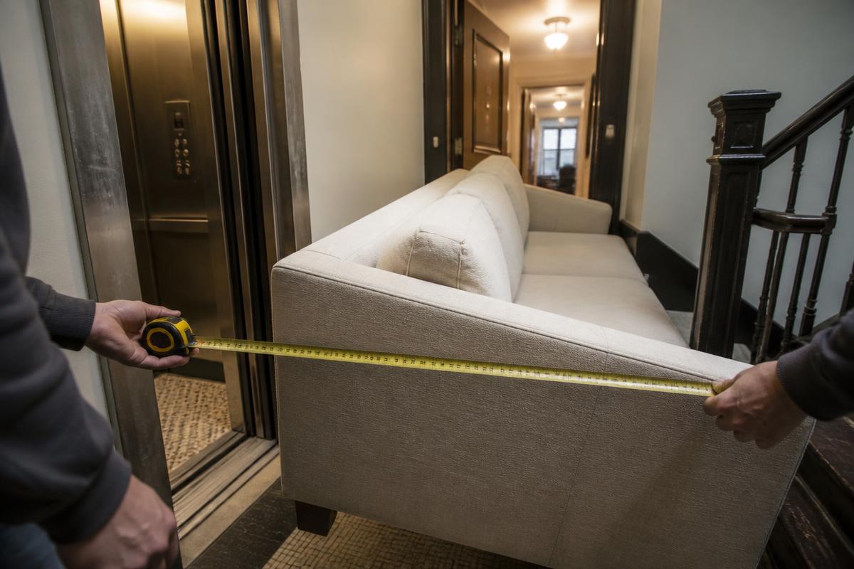 A sofa being measured through a tight apartment elevator-hallway turn