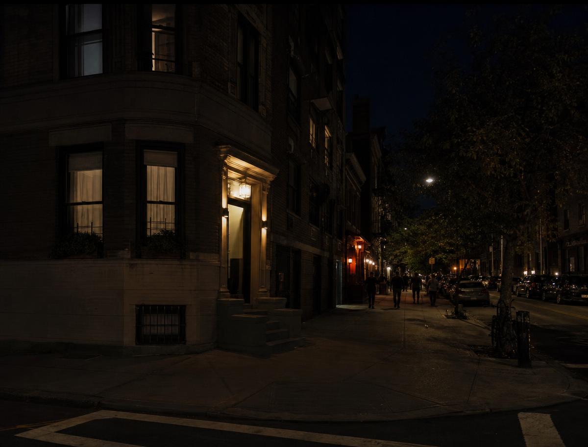 A quiet Manhattan corner building at night, lights on in a few apartments