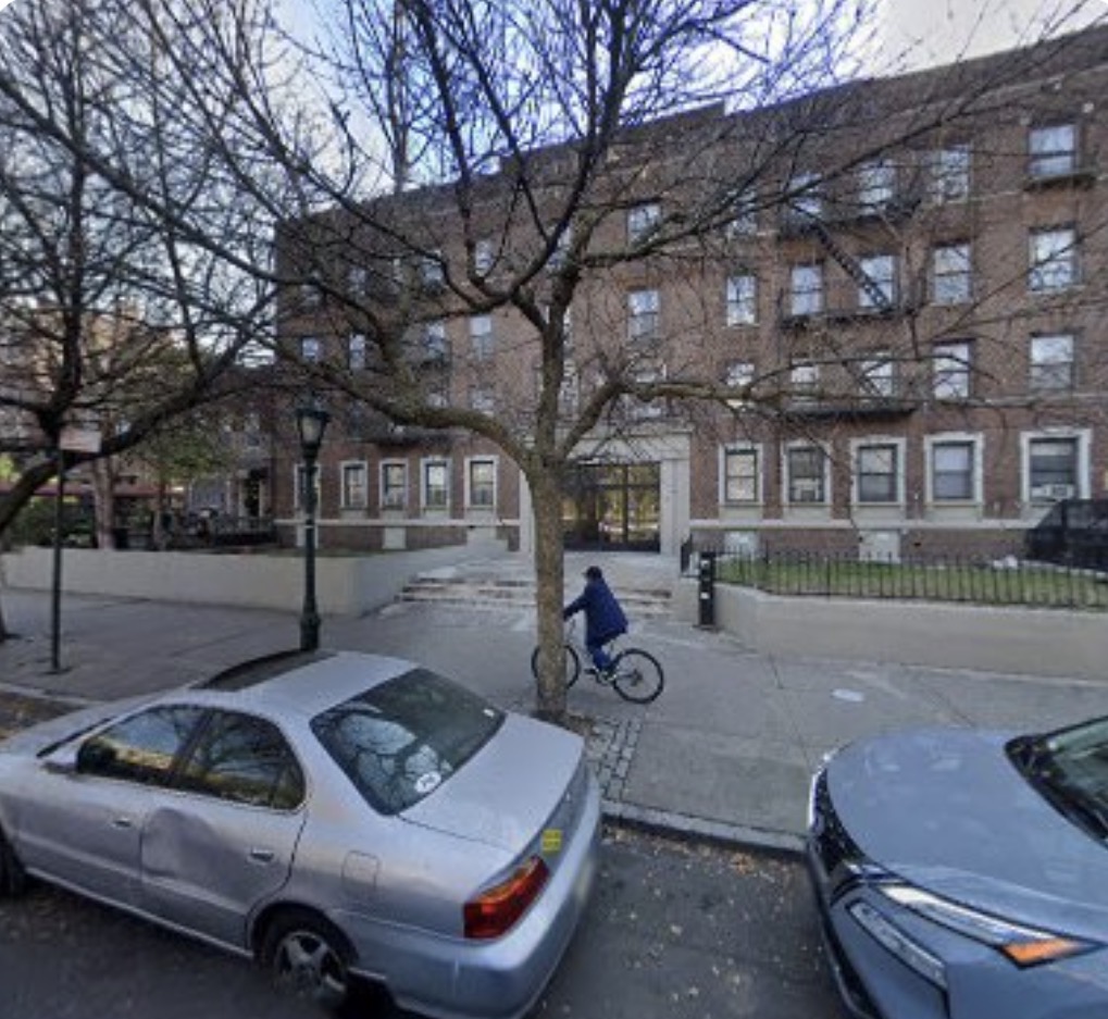 A four-story prewar brick apartment building on Eastern Parkway in Crown Heights, Brooklyn, with fire escapes and bare trees along the sidewalk
