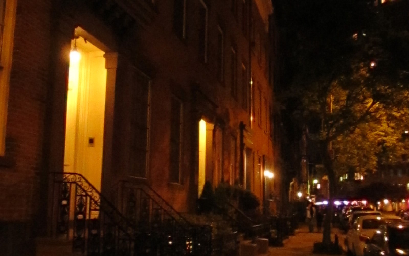 A residential street in Greenwich Village at night, stoop lights on and windows lit above the sidewalk.