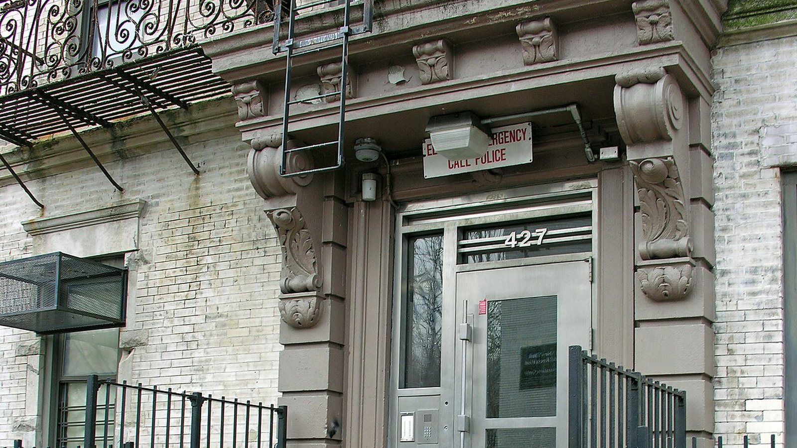 Entrance of a worn Bronx apartment building with a fire escape and an 'Emergency Call Police' sign — the reality inside Pinnacle's former rent-stabilized portfolio.